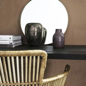 Vase Etnik rouge violet en laiton posé sur un meuble noir avec miroir rond et chaise en rotin - House Doctor - Woodely